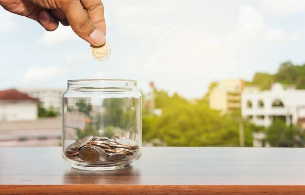 Someone adding to a jar of coins; saving finances