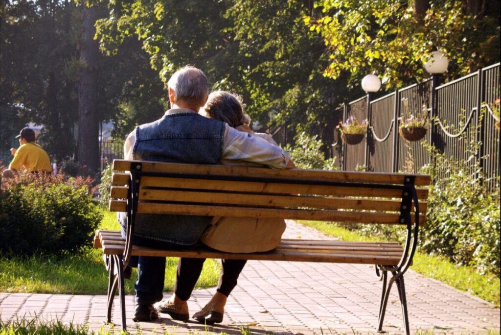 Two senior citizens sitting on a bench, facing away