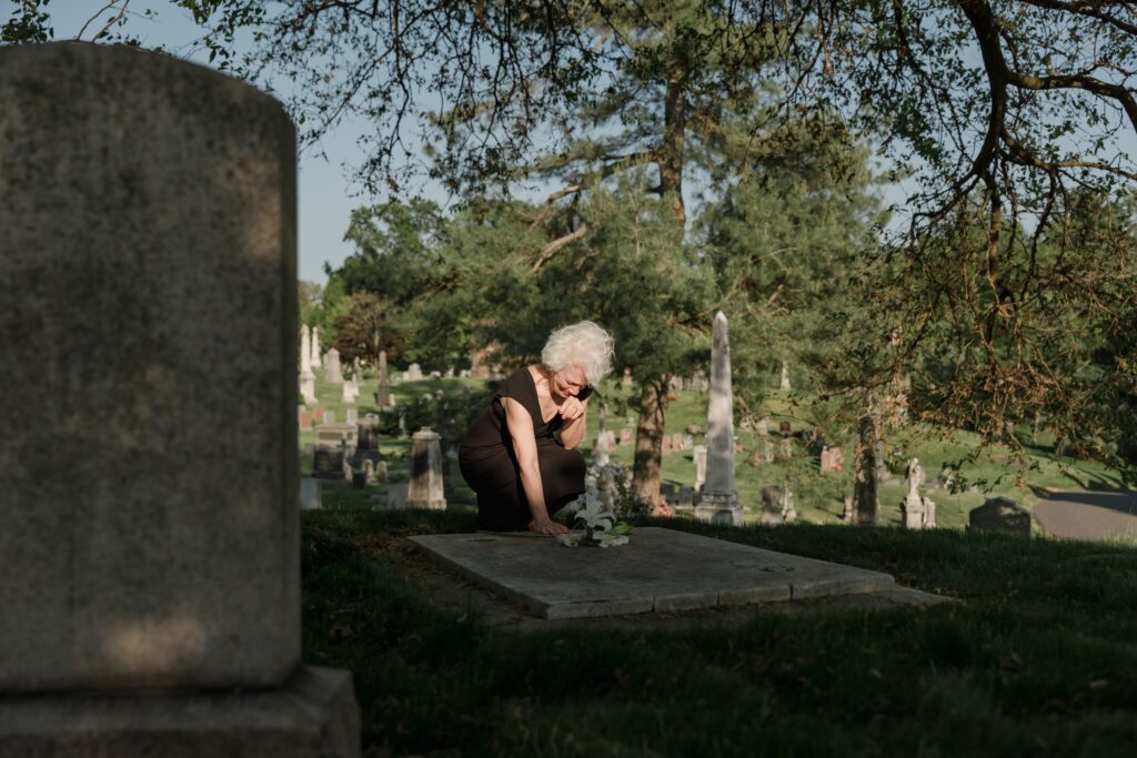 surviving spouses; elderly woman mourning; placing flowers on grave